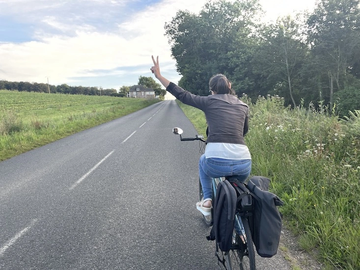 Photo d'une cycliste abordant une côte avec deux doigts levé en V en signe de facilité